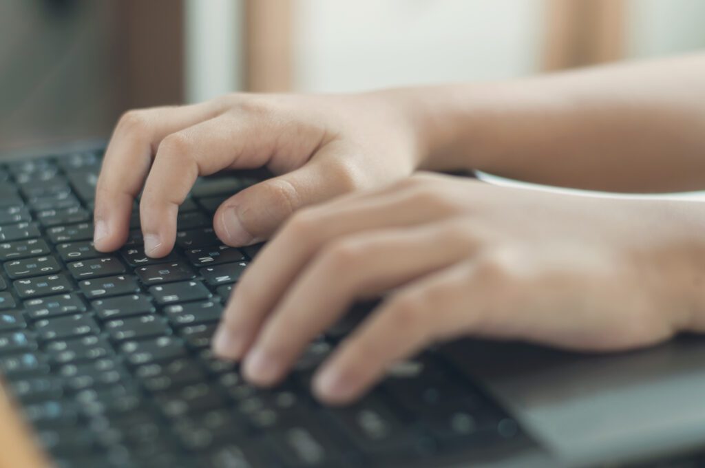 Hands of kid is typing on keyboard pad of computer